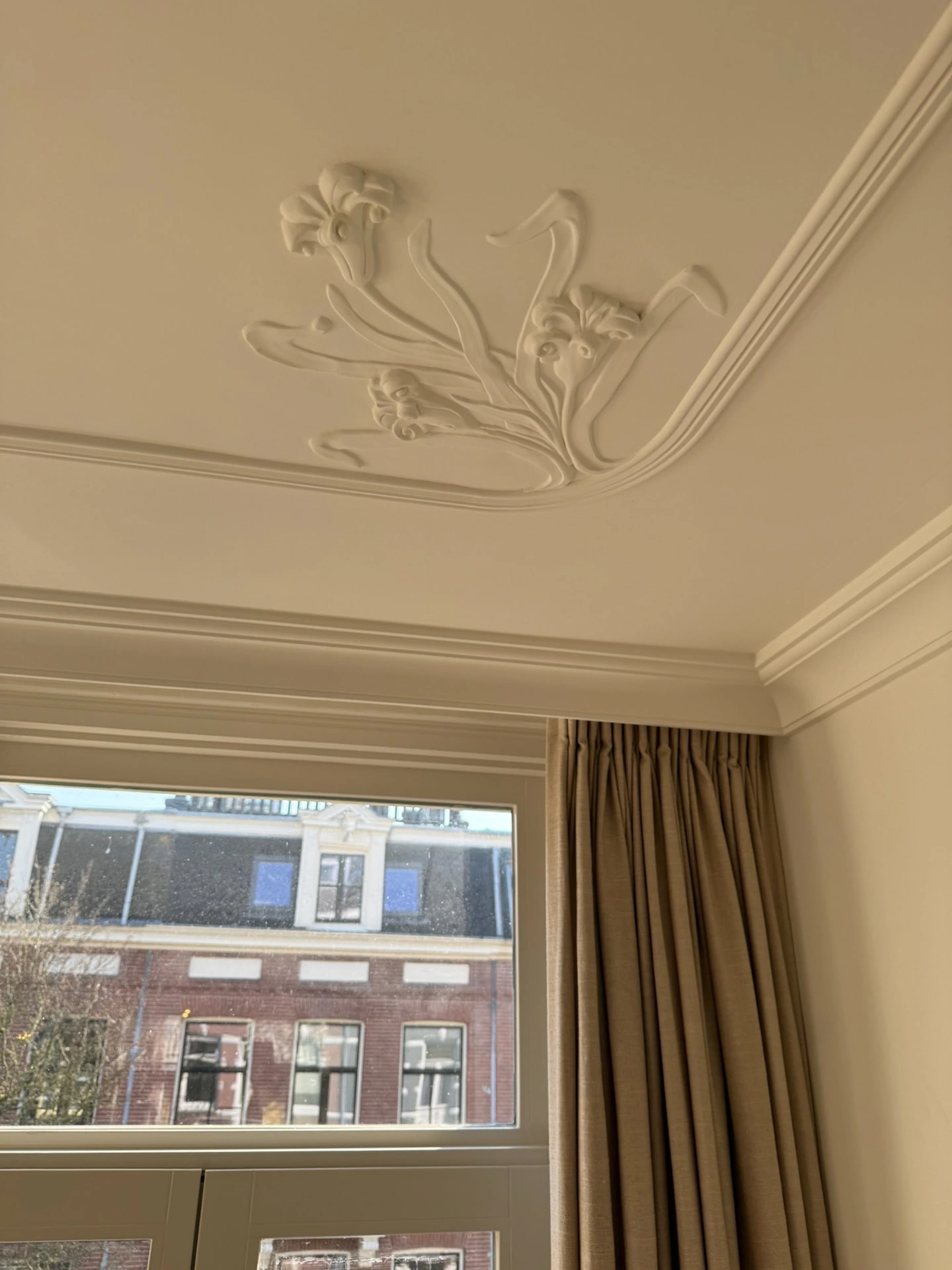 Decoratief plafondornament met bloemmotief boven een raam